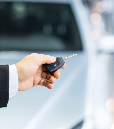 Drive carefully! Close up shoot of the hand holding car keys in front of a car